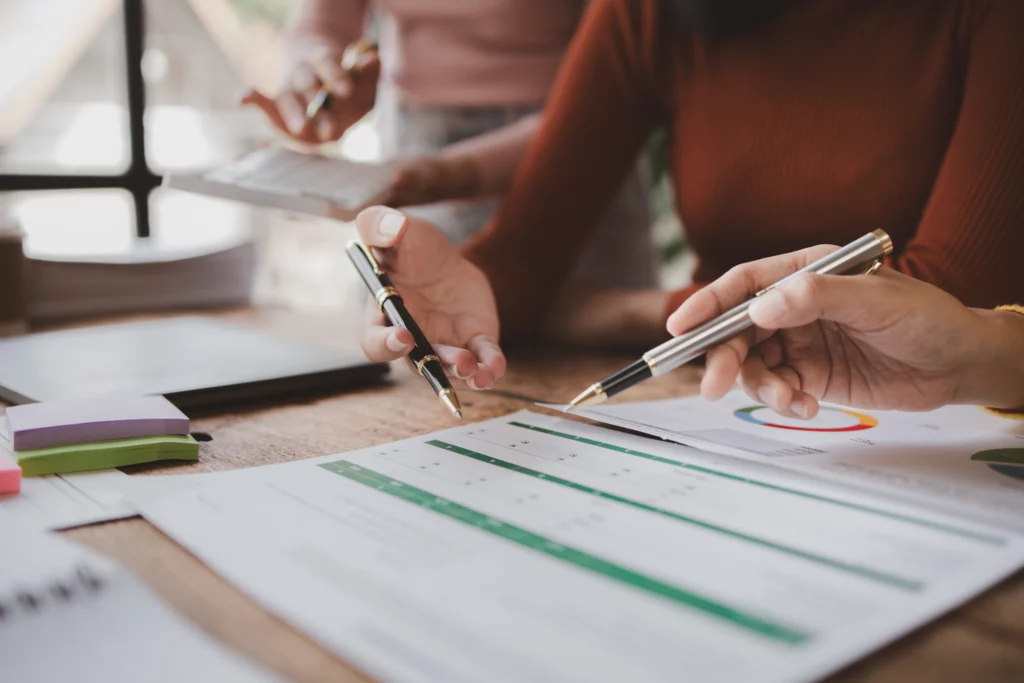 Three hands with pens point to financial graphs on paper in an office, symbolizing a focused discussion about co-signer protections.