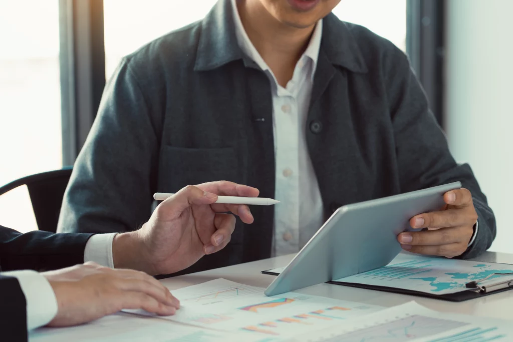 Two people review financial charts at a table; one holds a tablet while the other points with a stylus, symbolizing collaboration on bankruptcy plans.