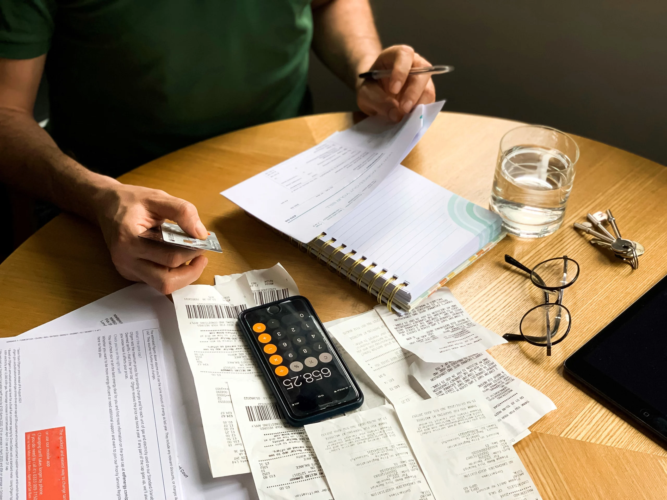 Person managing finances with bills, receipts, credit card, smartphone calculator, and notebook at a table, representing debt planning.