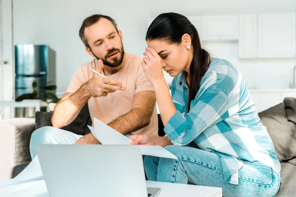 Man speaking to a distressed woman holding papers in a bright living room, representing financial stress and bankruptcy discussions in Maryland