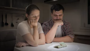 Worried couple at kitchen table looking at money and paperwork, showing financial stress