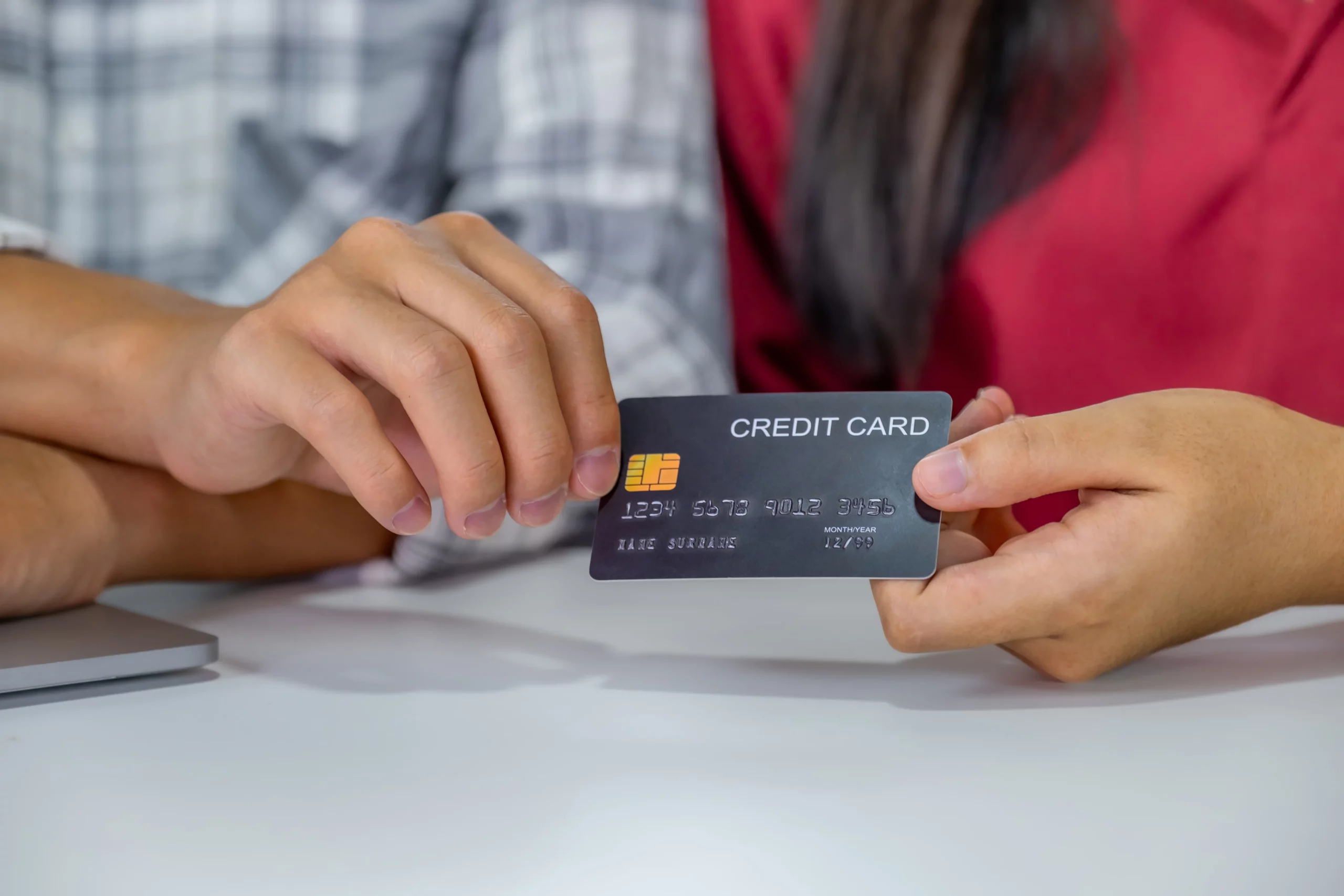 Two people holding a credit card together at a table, representing joint credit card responsibility and how shared debt is affected when one person files for bankruptcy in Maryland.