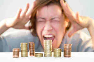 Stacks of coins in the foreground with a stressed person holding their head in the background, representing financial hardship and considering multiple bankruptcy filings in Maryland.