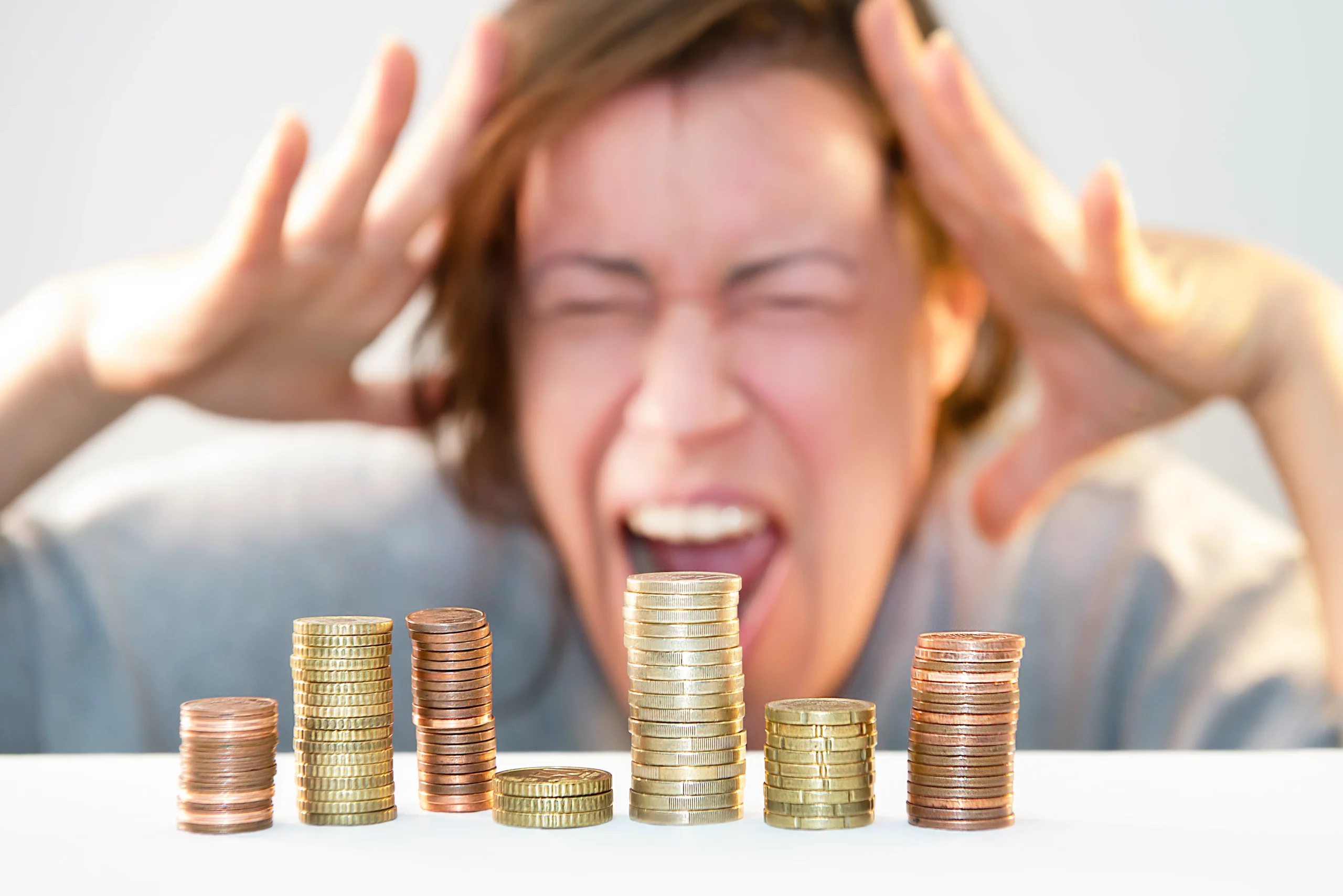 Stacks of coins in the foreground with a stressed person holding their head in the background, representing financial hardship and considering multiple bankruptcy filings in Maryland.