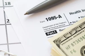 Tax Form 1095-A with cash, a calendar, and financial paperwork on a desk, representing tax debt concerns and the potential to discharge certain older tax debts through bankruptcy in Maryland.